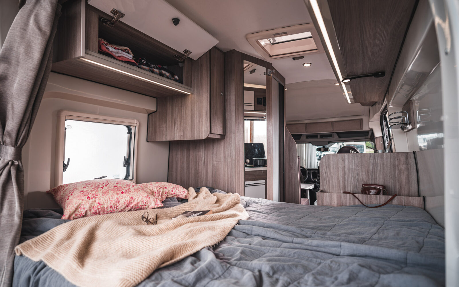 Intérieur du van aménagé avec un lit confortable et des draps colorés - Trip'in location de vans